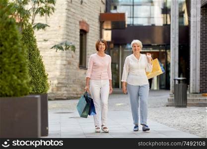 sale, consumerism and people concept - two senior women or friends with shopping bags walking along tallinn city street. senior women with shopping bags walking in city
