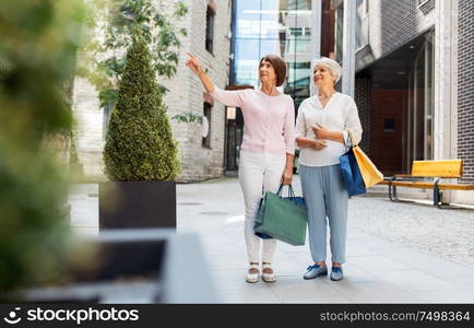 sale, consumerism and people concept - two senior women or friends with shopping bags on city street in tallinn. senior women with shopping bags walking in city