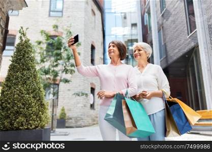 sale, consumerism and people concept - two senior women or friends with shopping bags taking selfie by smartphone on tallinn city street. old women with shopping bags taking selfie in city