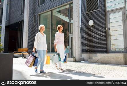 sale, consumerism and people concept - two senior women or friends with shopping bags walking along tallinn city street. senior women with shopping bags walking in city