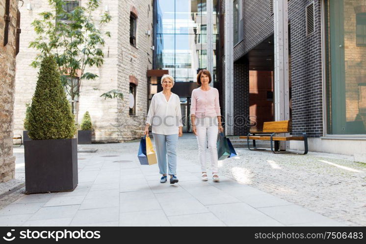 sale, consumerism and people concept - two senior women or friends with shopping bags walking along tallinn city street. senior women with shopping bags walking in city