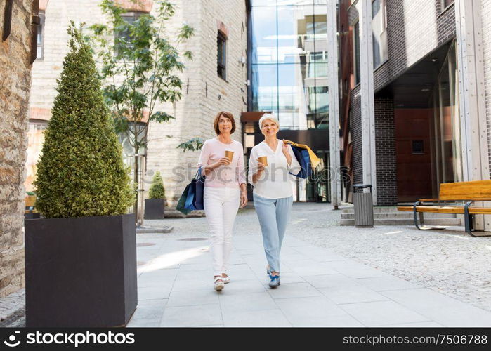 sale, consumerism and people concept - two senior women or friends with shopping bags drinking takeaway coffee and walking along tallinn city street. senior women with shopping bags and coffee in city