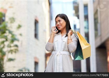 sale, consumerism and people concept - young asian woman with shopping bags calling on smartphone on city street. woman with shopping bags calling on smartphone