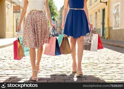 sale, consumerism and people concept - young women with shopping bags walking along city street. women with shopping bags walking in city