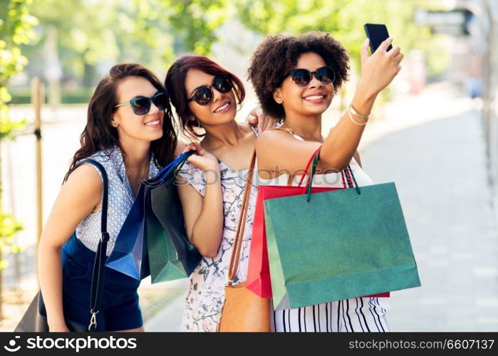 sale, consumerism and technology concept - happy young women with shopping bags taking selfie by smartphone in city. women with shopping bags taking selfie in city