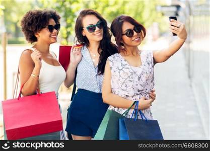 sale, consumerism and technology concept - happy young women with shopping bags taking selfie by smartphone in city. women with shopping bags taking selfie in city
