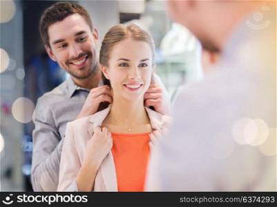 sale, consumerism, presents, holidays and people concept - happy couple trying golden pendant on at jewelry store in mall. couple trying golden pendant on at jewelry store