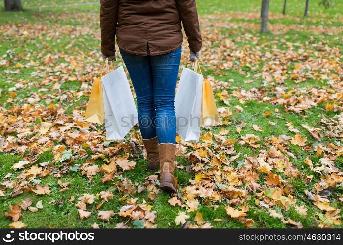 sale, consumerism, season and people concept - woman with shopping bags walking along autumn park