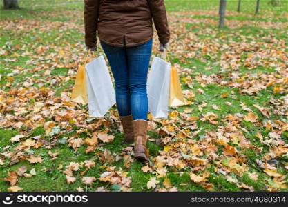 sale, consumerism, season and people concept - woman with shopping bags walking along autumn park