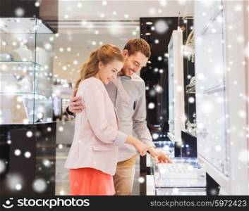 sale, consumerism, shopping and people concept - happy couple choosing engagement ring at jewelry store in mall with snow effect