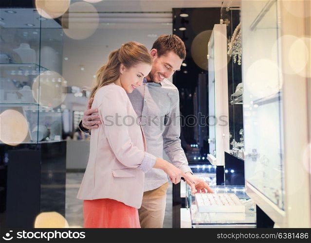 sale, consumerism, shopping and people concept - happy couple choosing engagement ring at jewelry store in mall. happy couple choosing engagement ring in mall