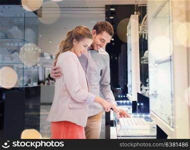 sale, consumerism, shopping and people concept - happy couple choosing engagement ring at jewelry store in mall. happy couple choosing engagement ring in mall