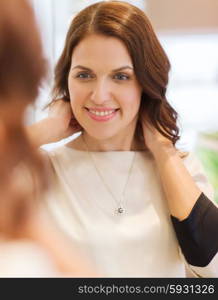 sale, consumerism, shopping and people concept - happy woman choosing and trying on pendant at jewelry store