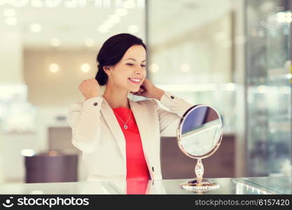 sale, consumerism, shopping and people concept - happy woman choosing and trying on pendant at jewelry store