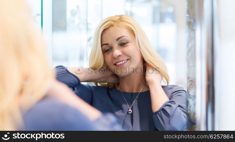 sale, consumerism, shopping and people concept - happy woman choosing and trying on pendant at jewelry store