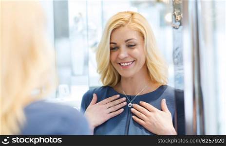 sale, consumerism, shopping and people concept - happy woman choosing and trying on pendant at jewelry store