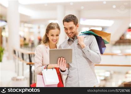 sale, consumerism, technology and people concept - happy young couple with shopping bags and tablet pc computer pointing finger in mall