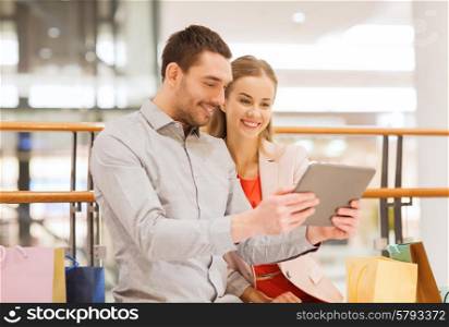 sale, consumerism, technology and people concept - happy young couple with shopping bags and tablet pc computer in mall