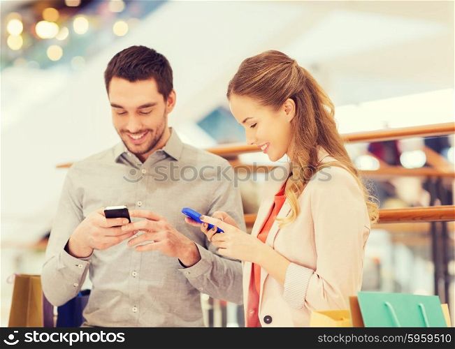 sale, consumerism, technology and people concept - happy young couple with shopping bags and smartphones in mall