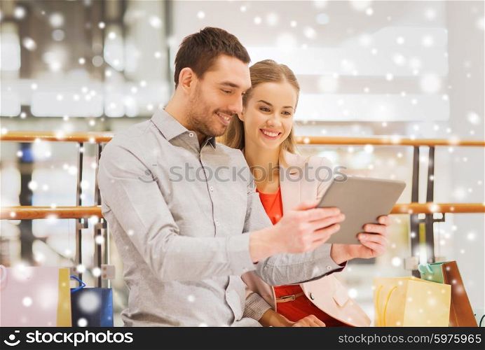 sale, consumerism, technology and people concept - happy young couple with shopping bags and tablet pc computer in mall with snow effect
