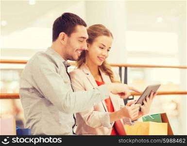 sale, consumerism, technology and people concept - happy young couple with shopping bags pointing finger to tablet pc computer in mall