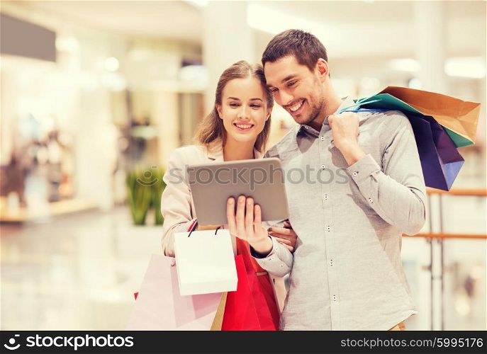 sale, consumerism, technology and people concept - happy young couple with shopping bags and tablet pc computer in mall