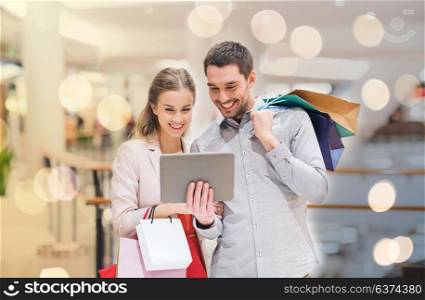 sale, consumerism, technology and people concept - happy young couple with shopping bags and tablet pc computer pointing finger in mall. couple with tablet pc and shopping bags in mall