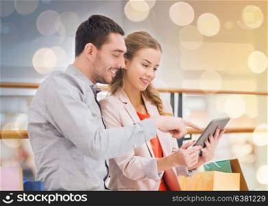 sale, consumerism, technology and people concept - happy young couple with shopping bags pointing finger to tablet pc computer in mall. couple with tablet pc and shopping bags in mall