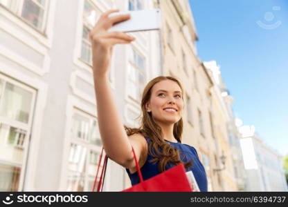 sale, consumerism, technology and people concept - happy young woman with shopping bags and smartphone taking selfie on city street. woman shopping and taking selfie by smartphone