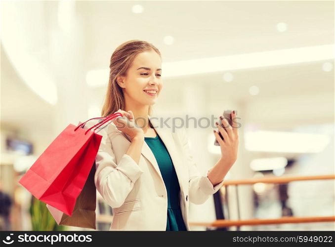 sale, consumerism, technology and people concept - happy young woman with smartphone and shopping bags taking selfie in mall