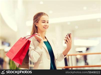 sale, consumerism, technology and people concept - happy young woman with smartphone and shopping bags taking selfie in mall
