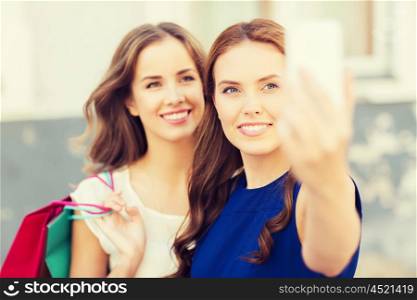 sale, consumerism, technology and people concept - happy young women with shopping bags and smartphone taking selfie on city street