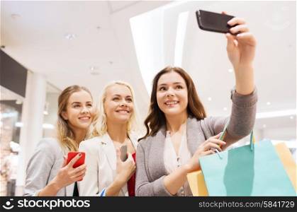 sale, consumerism, technology and people concept - happy young women with smartphones and shopping bags taking selfie in mall