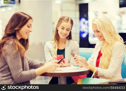 sale, consumerism, technology and people concept - happy young women with smartphones and shopping bags in mall