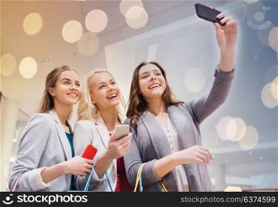 sale, consumerism, technology and people concept - happy young women with smartphones and shopping bags taking selfie in mall. women with smartphones shopping and taking selfie