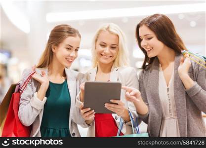 sale, consumerism, technology and people concept - happy young women with tablet pc and shopping bags in mall