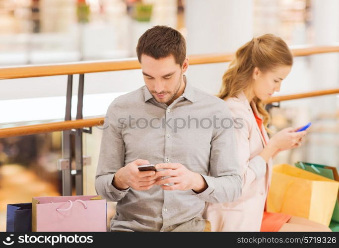 sale, consumerism, technology and people concept - young couple with shopping bags and smartphones in mall