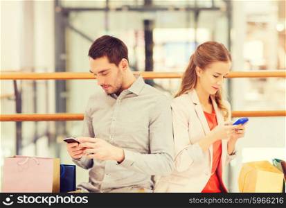 sale, consumerism, technology and people concept - young couple with shopping bags and smartphones in mall