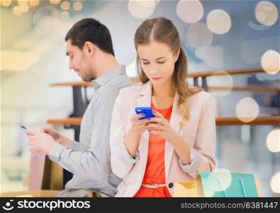 sale, consumerism, technology and people concept - young couple with shopping bags and smartphones in mall. couple with smartphones and shopping bags in mall