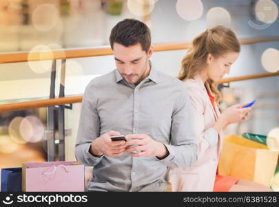 sale, consumerism, technology and people concept - young couple with shopping bags and smartphones in mall. couple with smartphones and shopping bags in mall