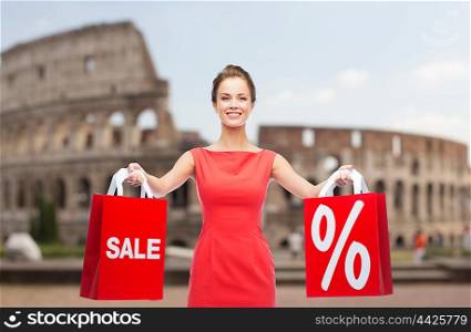 sale, discount, tourism and holidays concept - smiling young woman in red dress with shopping bags with percent sign over coliseum background