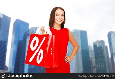 sale, discount, tourism and holidays concept - smiling young woman in red dress with shopping bags with percent sign over singapore city skyscrapers background