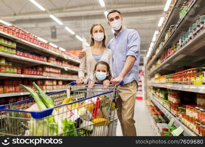 sale, family and pandemic concept - happy mother, father and daughter wearing face protective medical masks for protection from virus disease with shopping cart buying food at supermarket. family with shopping cart in masks at supermarket