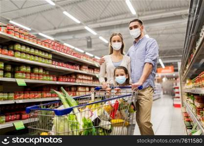 sale, family and pandemic concept - happy mother, father and little daughter wearing face protective medical masks for protection from virus disease with shopping cart buying food at supermarket. family with shopping cart in masks at supermarket
