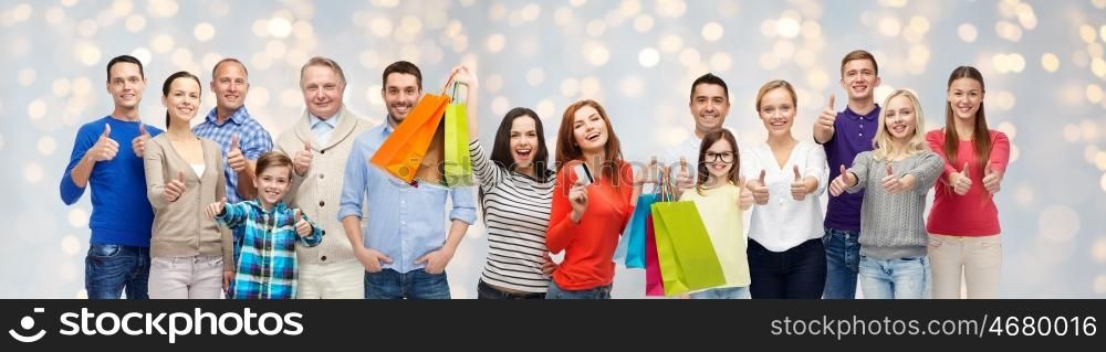 sale, family, generation and people concept - group of happy men and women with shopping bags and credit card showing thumbs up over holidays lights background