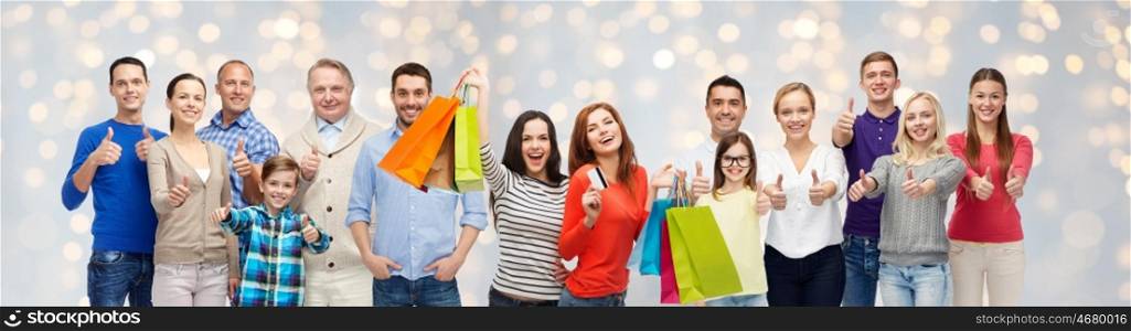 sale, family, generation and people concept - group of happy men and women with shopping bags and credit card showing thumbs up over holidays lights background
