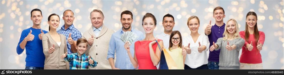 sale, family, generation and people concept - group of happy men and women with shopping bags and money showing thumbs up over holidays lights background