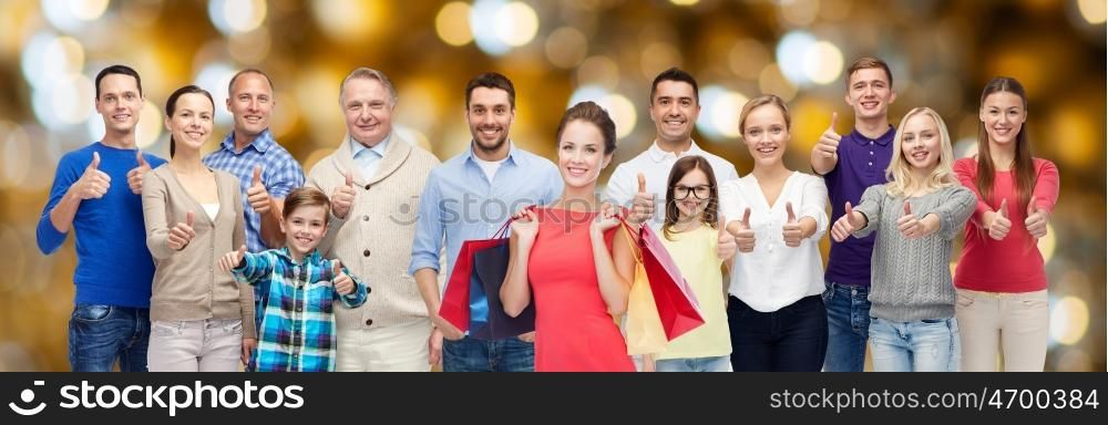 sale, family, generation and people concept - group of happy men and women with shopping bags showing thumbs up over holidays lights background