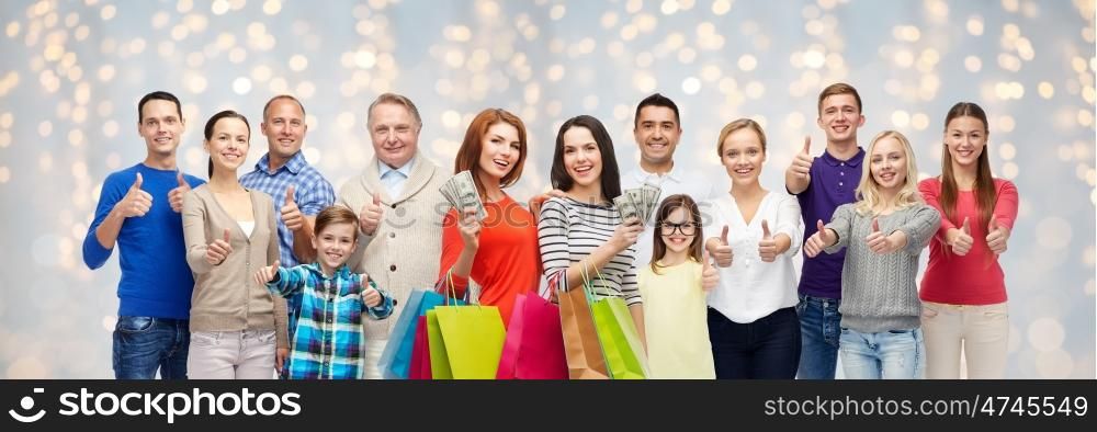 sale, family, generation and people concept - group of happy men and women with shopping bags and money showing thumbs up over holidays lights background