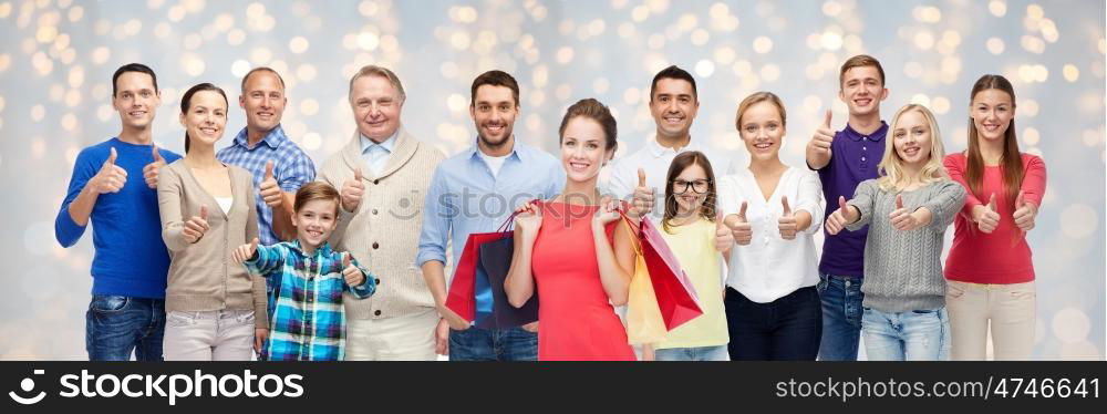 sale, family, generation and people concept - group of happy men and women with shopping bags showing thumbs up over holidays lights background